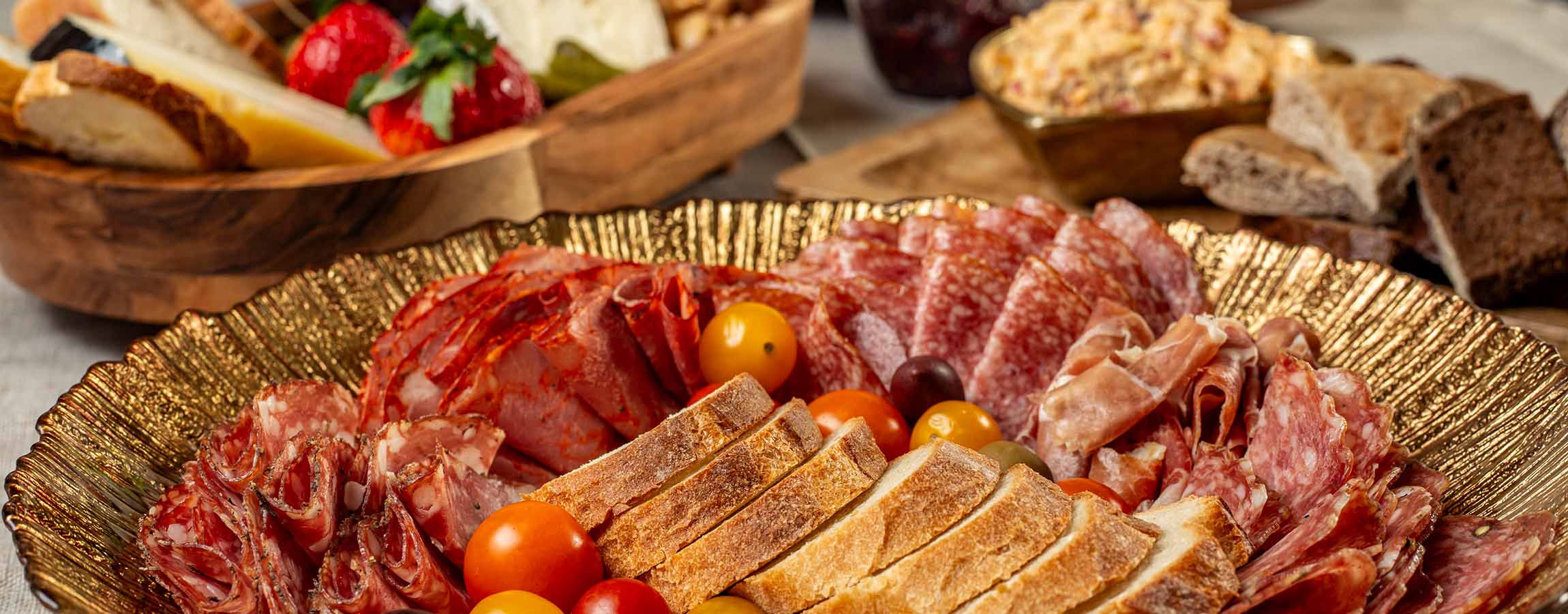 Array of sliced deli meat, bread and tomatoes in a decorative bowl.